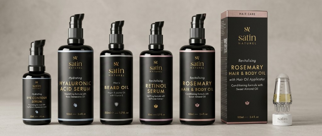 Satin Naturel product family on neutral grey — hydrating serums, beard oil, retinol serum, rosemary hair and body oil with carton and hair oil applicator